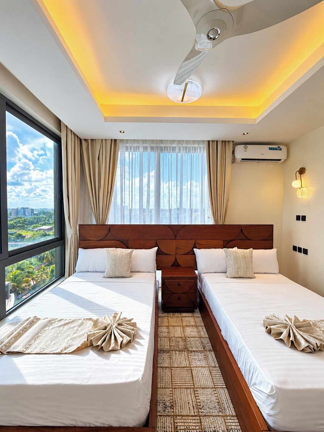 Une chambre d’hôtel avec deux lits, une grande fenêtre, un climatiseur et un ventilateur de plafond.