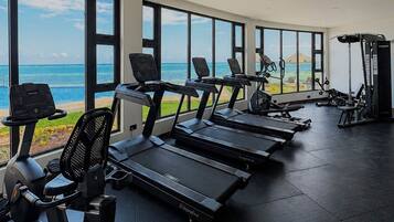 A gym with treadmills and exercise equipment, large windows with a view of the ocean.