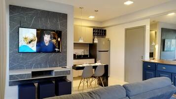 Una sala de estar moderna con un televisor de pantalla plana, un sofá gris y una zona de cocina con una mesa y sillas.