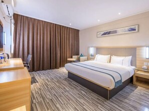 Una habitación de hotel con una cama grande, un escritorio, una silla, una mesita de noche y un amplio ventanal con cortinas.