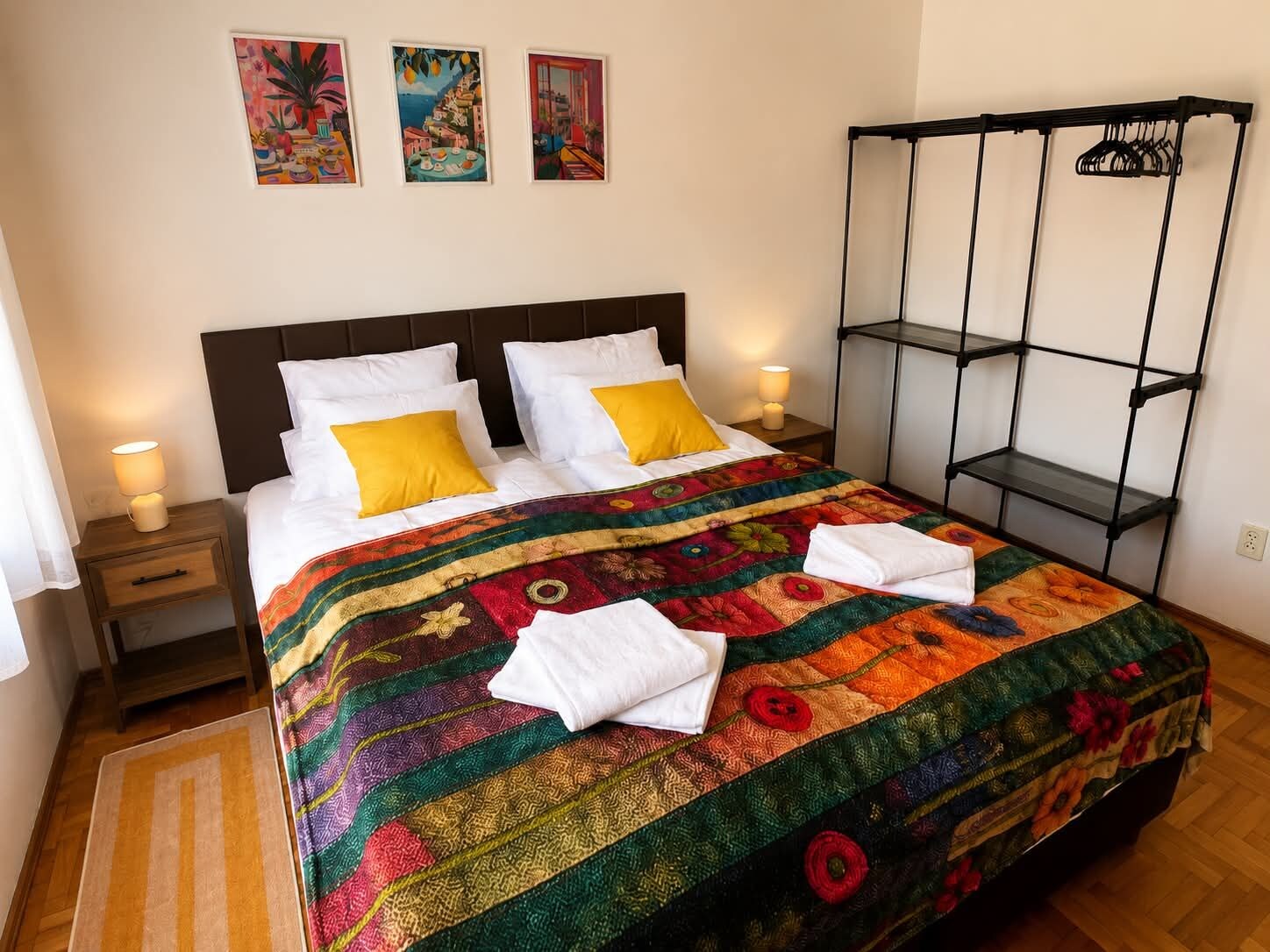 A bed with a colorful quilt, two bedside lamps, and a black metal shelf unit.