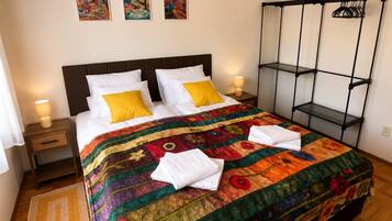 A bed with a colorful quilt, two bedside lamps, and a black metal shelf unit.