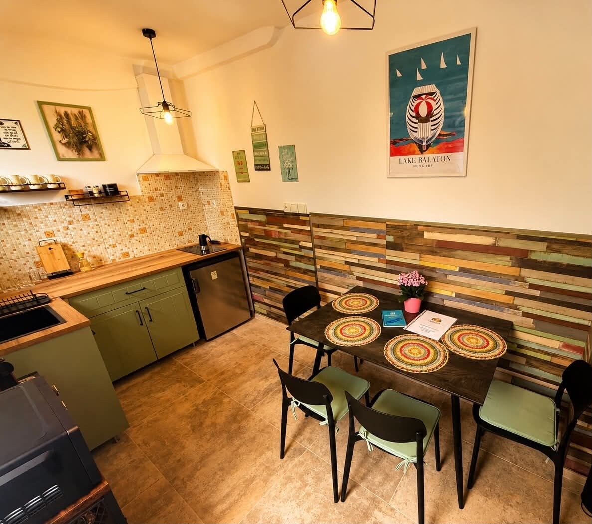 Una cucina compatta con zona pranzo, caratterizzata da una parete di fondo rivestita in piastrelle, una lampada a sospensione moderna e un elemento decorativo a parete.
