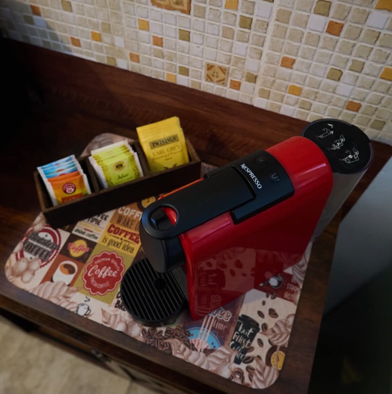 A coffee machine with a red and black design, a tray with coffee pods, and a coffee-themed placemat.