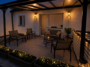 Een terras buiten met zitplaatsen, een tafel en decoratieve verlichting.