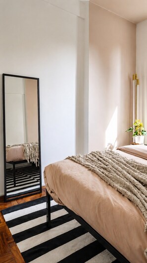 Ein Schlafzimmer mit einem Bett, einem schwarz-weißen Teppich, einem Spiegel und einem Nachttisch mit einer Pflanze.