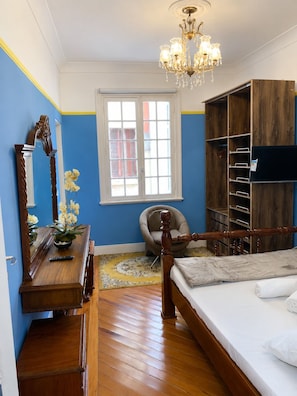 Un dormitorio con cama de madera, cómoda, silla, ventana grande y candelabro.