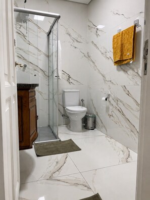 Un baño con cabina de ducha de vidrio, inodoro y pared con diseño de mármol.