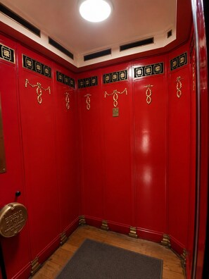 En rød elevator med guld detaljer, et metalgreb og en lille skilt på væggen.