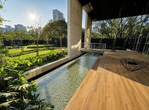 A modern outdoor area with a clear water feature, wooden flooring, and a seating area with a unique metal chair design. - Ao lado da Av. Paulista | Metrô Paraíso | Moderno (São Paulo)