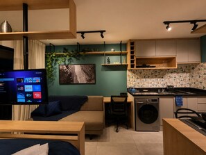 A compact living space with a kitchenette, a sofa, a TV, and a washing machine. - Personalidade e Estilo | Ao lado do Sírio-Libanês (São Paulo)