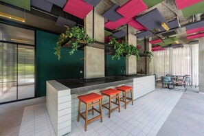 A modern bar area with a white countertop, three wooden stools with orange cushions, and hanging plants. - Praticidade a 1 minuto do Metrô República (Santa Ifigênia)