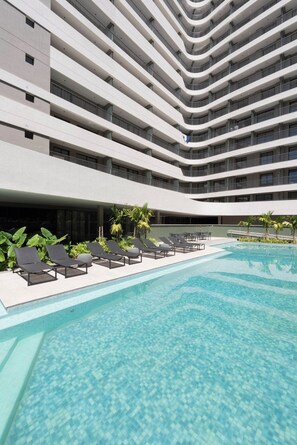 A modern hotel with a pool area, multiple balconies, and lounge chairs. - Praticidade a 1 minuto do Metrô República (Santa Ifigênia)