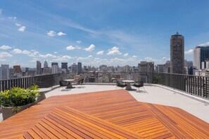A rooftop terrace with a wooden deck, outdoor seating, and a city skyline view. - Conforto para até 4 pessoas | Metrô República (Santa Ifigênia)