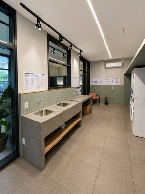 A modern bathroom with a granite sink, a mirror, and a built-in washing machine. - Conforto para até 4 pessoas | Metrô República (Santa Ifigênia)