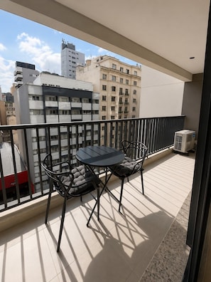 Un balcon avec une table et des chaises, une vue sur les bâtiments et un appareil de climatisation.