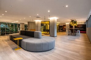 A modern interior with a curved grey sofa, a yellow side table, and a bar area with stools. - Av. Paulista | Metrô Paraíso | Conforto e Lazer (São Paulo)