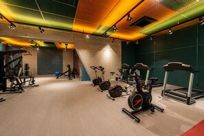 Ein Fitnessstudio mit unterschiedlichen Trainingsgeräten, darunter Laufbänder und Ergometer, unter einer Decke mit Musterbeleuchtung.