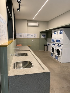Eine öffentliche Toilette mit zwei Waschbecken, einem Mülleimer und einer Waschmaschine.