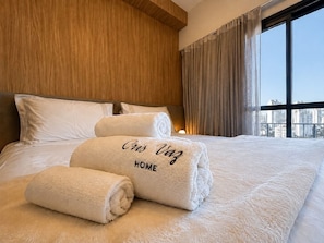 Ein Hotelzimmer mit einem großen Bett, einem Holzkopfstück und Blick auf die Stadt durch das Fenster.
