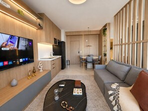 Ein modernes Wohnzimmer mit Flachbildfernseher, einer Couch, einem Couchtisch und einem Essbereich mit Tisch und Stühlen.