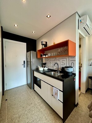 A compact kitchen with a refrigerator, stove, and a shelf with glasses. - Refúgio na Rua Augusta | Varanda e Ar Condicionado (São Paulo)