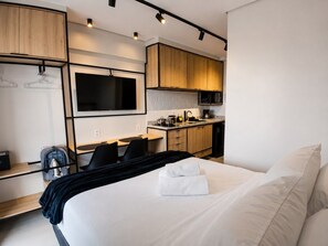 Een moderne hotelkamer met een bed, een bureau, een stoel, een kitchenette en een televisie.