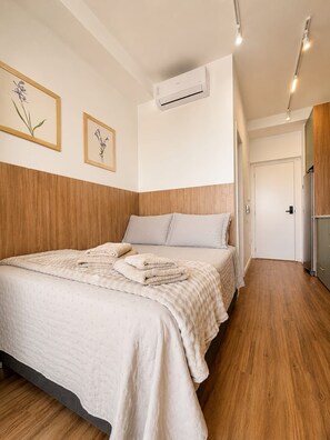 Ein Schlafzimmer mit einem Bett, Holzwandverkleidung, einer Klimaanlage und einer Tür zu einem weiteren Raum.