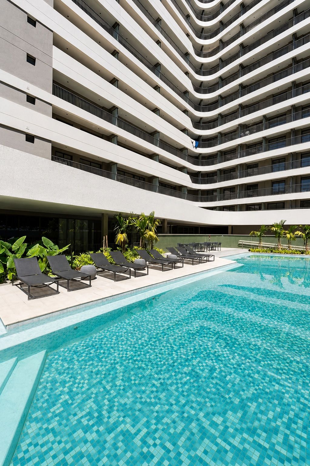 A modern hotel with a multi-level pool area, lounge chairs, and a clear blue pool.