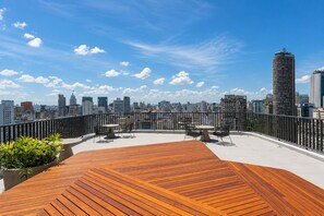 Eine Dachterrasse mit einer Holzdielen-Terrasse, Sitzgelegenheiten im Freien und Blick auf eine Stadtlandschaft.
