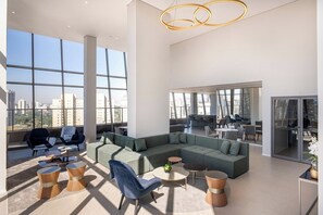 A spacious living area with a sectional sofa, round coffee tables, and comfortable seating. - Vista aberta | Luz natural 650m do Metrô Brooklin (São Paulo)