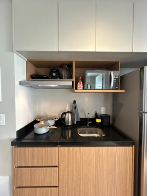 A compact kitchen with a microwave, stove, and sink. - Vista aberta | Luz natural 650m do Metrô Brooklin (São Paulo)