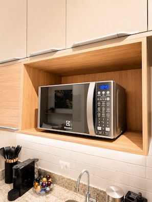 A modern kitchen with a built-in Electrolux microwave on a wooden shelf, a granite countertop, and a stainless steel sink. - Conforto | Estilo | Metrô República (Santa Ifigênia)