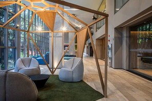 Ein modernes Interieur mit einer geometrischen Holzkonstruktion, Sitzbereichen und großen Fenstern.