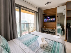 Ein Hotelzimmer mit Bett, Schreibtisch, Stuhl, Fernseher und Blick auf die Stadt.