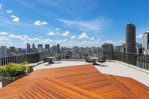 Eine Dachterrasse mit einer Holzdielen-Terrasse, Sitzgelegenheiten im Freien und Blick auf eine Stadtlandschaft.