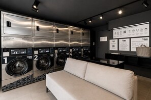 Eine moderne Waschküche mit mehreren Waschmaschinen, einer Couch und Informationsplakaten an der Wand.