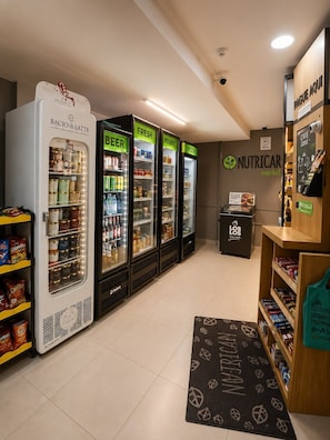 A grocery store with refrigerated sections labeled 'Beer,' 'Fresh Foods,' and 'Frozen.' There are shelves with packaged goods and a display for 'Los Los' coffee. - Moderno e Equipado | 1 Vaga | Metrô República (São Paulo)