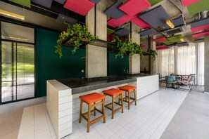 A modern bar area with a white counter, three wooden stools with orange cushions, and colorful ceiling panels. - Centro São Paulo, República, 3 min do metrô (Santa Ifigênia)