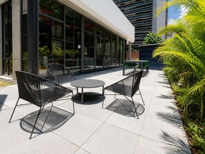Un espace extérieur aménagé avec une table ronde et deux chaises, entouré d’un petit muret et de plantes en pot.