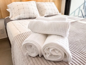 A neatly made bed with rolled white towels and a quilted blanket. - Centro São Paulo, República, 3 min do metrô (Santa Ifigênia)