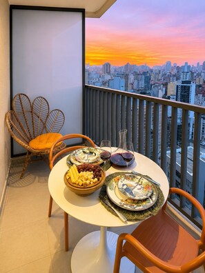 A balcony with a cityscape view, a round table with plates and glasses, and wicker chairs. - Vista | Centro SP | Metrô República (Santa Ifigênia)