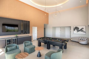 Uma sala de estar moderna com mesa de bilhar, assentos confortáveis, TV de tela plana e sofá.