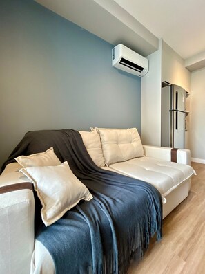 Ein modernes Wohnzimmer mit einer Couch, Kissen, einer Decke, einer Klimaanlage und einem Kühlschrank.