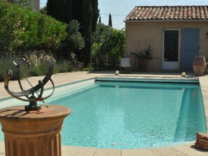 A swimming pool with a sun dial, surrounded by a garden and a building with a tiled roof. - Villa in Var With Swimming Pool (Cotignac)