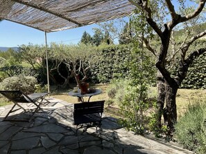 An outdoor patio with a stone floor, a round table with a potted plant, and a metal bench. - Villa in Var With Swimming Pool (Cotignac)