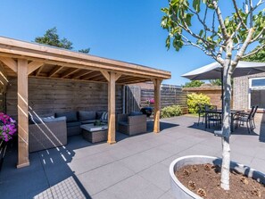 An outdoor patio area with a covered seating area, a dining table, and a small tree. - Holiday Home in Renesse With Swimming Pool (Renesse)