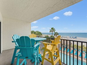 A balcony with a view of the beach, featuring outdoor seating and a pool. - Sandy Shores #202 (Madeira Beach)