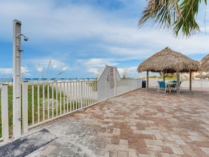 A paved patio with a white fence, a thatched umbrella, and a view of the sea. - Sandy Shores #202 (Madeira Beach)