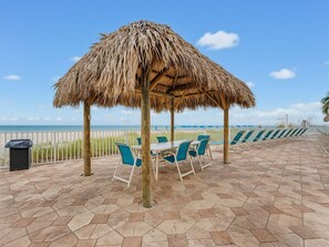 A beachside patio with a thatched roof, hexagonal stone flooring, and outdoor seating. - Sandy Shores #202 (Madeira Beach)